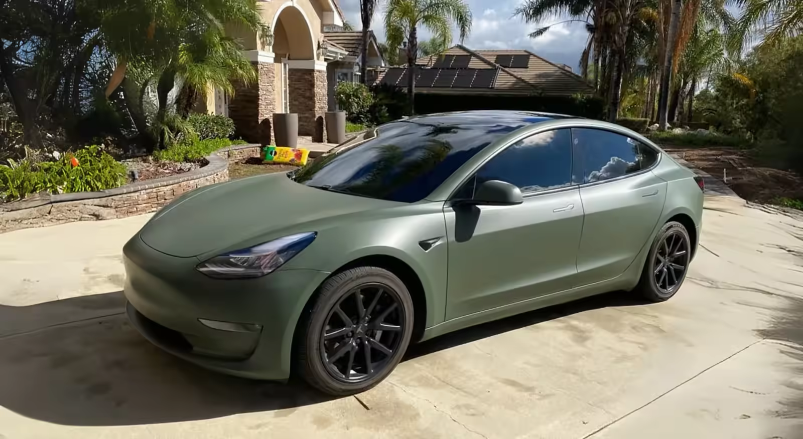Sage green Tesla with tinted windows outside a home